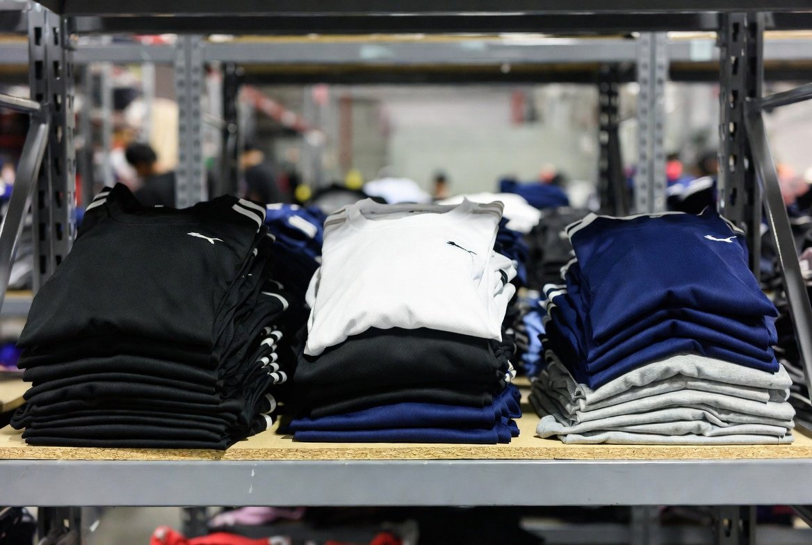Folded sports jerseys and dry-fit tops in various colours on shelving